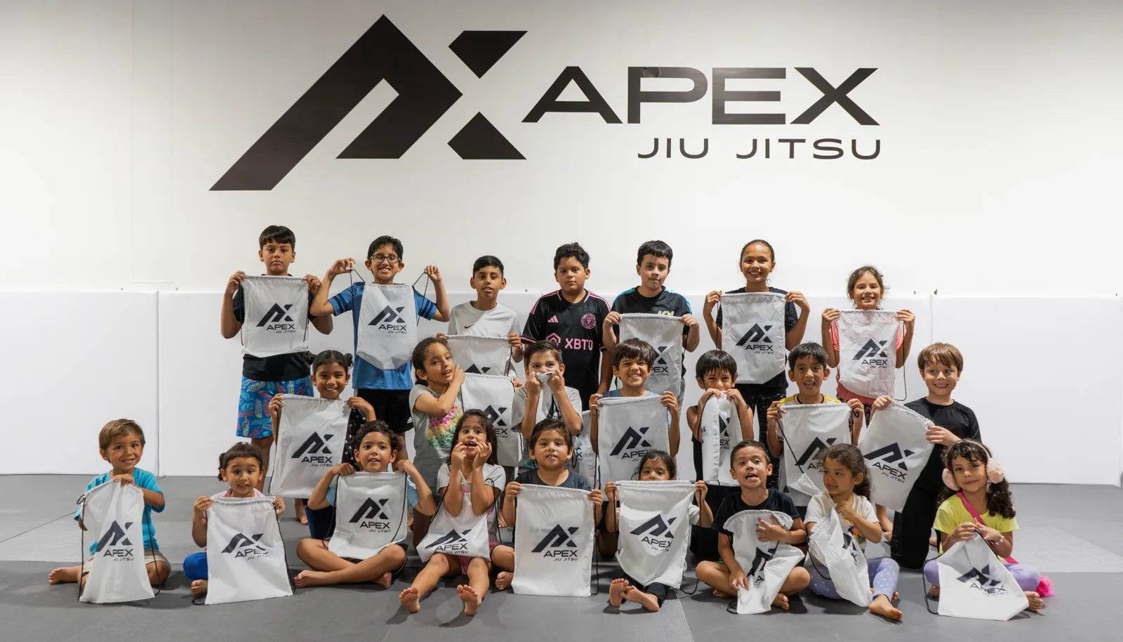 Grupo grande de niños de APEX frente al logo de la academia