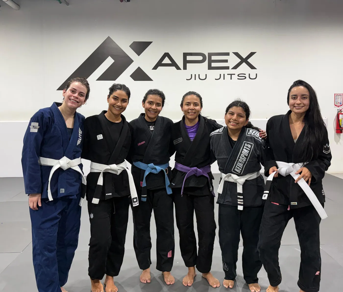 Alumnas del programa Femenino de APEX de pie, en kimono, frente al logo de la academia